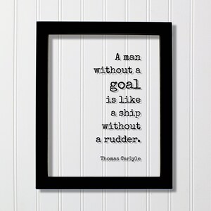 May include: Black framed print with a white background and a quote in black text: "A man without a goal is like a ship without a rudder." The quote is attributed to Thomas Carlyle.