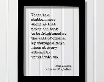 May include: A black rectangular frame containing a white print with the black typewriter-style text: There is a stubbornness about me that never can bear to be frightened at the will of others. My courage always rises at every attempt to intimidate me. Jane Austen, Pride and Prejudice.
