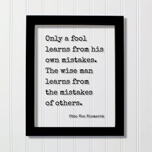 May include: A black rectangular frame containing a white print with the black typewriter-style text: Only a fool learns from his own mistakes. The wise man learns from the mistakes of others. Otto Von Bismarck is printed at the bottom right.