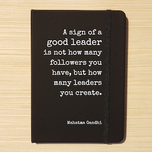 May include: Black notebook with a white quote by Mahatma Gandhi: "A sign of a good leader is not how many followers you have, but how many leaders you create."