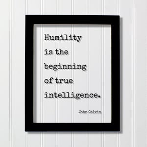 May include: A rectangular black frame containing a white print with the black typewriter-style text: Humility is the beginning of true intelligence. John Calvin. The quote is centered, and the author's name is positioned in the bottom right corner.