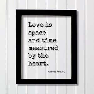 May include: Black framed print with a white background and a quote in black text that reads "Love is space and time measured by the heart." The quote is attributed to Marcel Proust.