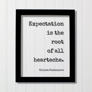 以下が含まれることがあります： 黒い長方形のフレームに、タイプライター風の黒い文字で「Expectation is the root of all heartache. William Shakespeare.」と書かれた白いプリントが入っています。フレームはシンプルで清潔感のあるデザインで、白い縦縞のパネルの前に配置されています。