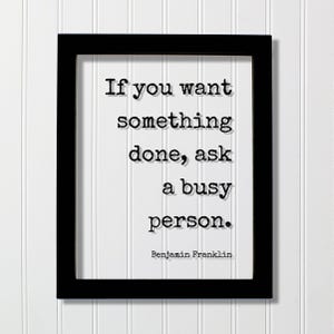 以下が含まれることがあります： 黒い長方形のフレームに、タイプライター風の黒い文字で「If you want something done, ask a busy person.」と書かれた白いプリントが入っています。白い紙の下部には、より小さな黒い文字でBenjamin Franklinと印刷されています。