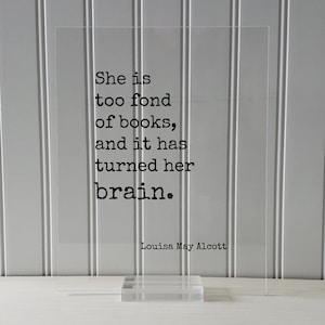 May include: A clear acrylic sign with a black quote that reads "She is too fond of books, and it has turned her brain." The quote is attributed to Louisa May Alcott.