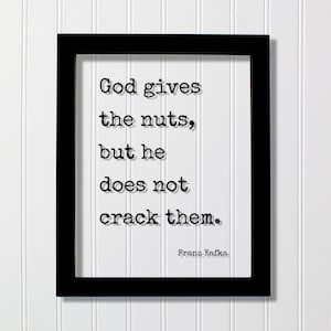 May include: Black framed print with a white background and black text that reads "God gives the nuts, but he does not crack them."  The text is attributed to Franz Kafka.