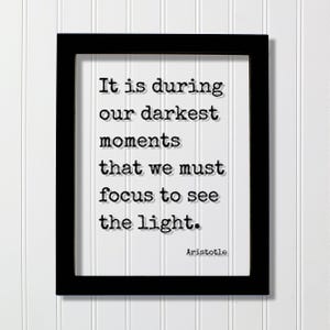 以下が含まれることがあります： 黒い長方形のフレームに、タイプライター風の黒い文字で「It is during our darkest moments that we must focus to see the light.」と書かれた白いプリントが入っています。右下隅には「Aristotle」という名前が印刷されています。