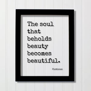 May include: A black rectangular frame containing a white print with the black typewriter-style text: The soul that beholds beauty becomes beautiful. The name Plotinus is printed in the bottom right corner of the white paper inside the frame.