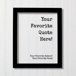 May include: A rectangular black picture frame containing a clear insert with black text that reads Your Favorite Quote Here! followed by smaller text at the bottom that reads Your Favorite Author! and Your Favorite Book! in a typewriter font.