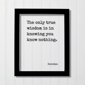 May include: A black rectangular frame containing a white print with the black text: The only true wisdom is in knowing you know nothing. The name Socrates is printed in the bottom right corner in a typewriter-style font on a white background.
