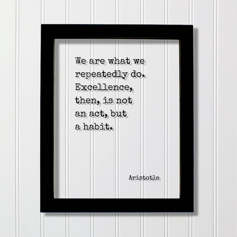Op de afbeelding: Zwart ingelijst print met een witte achtergrond en een citaat van Aristoteles in zwarte tekst: "We zijn wat we herhaaldelijk doen. Uitmuntendheid is dan geen daad, maar een gewoonte."