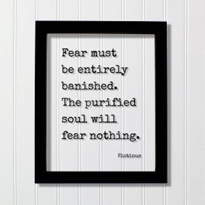 May include: A black rectangular frame containing a white print with black typewriter-style text that reads: Fear must be entirely banished. The purified soul will fear nothing. Plotinus. The lettering features a subtle drop shadow effect.