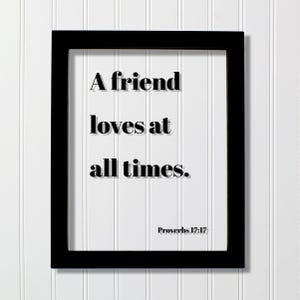 Op de afbeelding: Een rechthoekige zwarte lijst met een witte inzet waarop de zwarte tekst A friend loves at all times. en de referentie Proverbs 17:17 in een duidelijk, vet, schreefloos lettertype zijn gedrukt. Het ontwerp heeft een strakke, contrastrijke uitstraling.