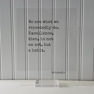 Op de afbeelding: Een transparante acrylplaat met een zwart citaat van Aristoteles: "We zijn wat we herhaaldelijk doen. Excellentie is dan geen daad, maar een gewoonte."