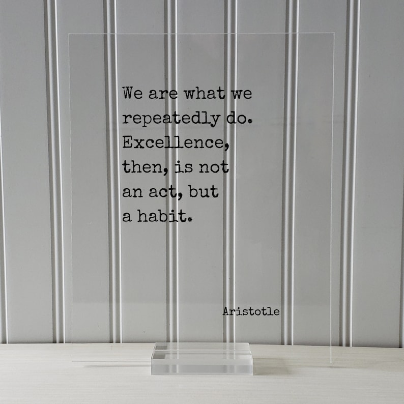 Op de afbeelding: Een transparante acrylplaat met een zwart citaat van Aristoteles: "We zijn wat we herhaaldelijk doen. Excellentie is dan geen daad, maar een gewoonte."