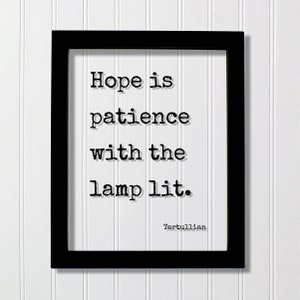 May include: Black framed wall art with the quote "Hope is patience with the lamp lit." in a typewriter font. The quote is attributed to Tertullian. The background is white.