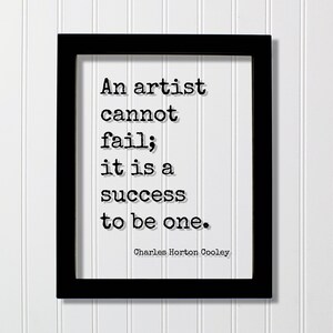 May include: A framed print with the quote "An artist cannot fail; it is a success to be one." by Charles Horton Cooley. The text is in black against a white background, framed in a black rectangular frame.