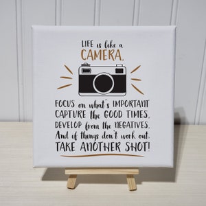 Puede incluir: Lienzo blanco con una ilustración en blanco y negro de una cámara y el texto "LIFE is like a CAMERA, FOCUS on what's IMPORTANT CAPTURE the GOOD TIMES, DEVELOP from the NEGATIVES. And if things don't work out. TAKE ANOTHER SHOT!"