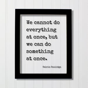 May include: Black framed print with a white background and a quote in black text: "We cannot do everything at once, but we can do something at once." The quote is attributed to Calvin Coolidge.