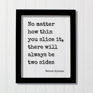 Op de afbeelding: Een zwarte rechthoekige lijst met een witte print met de zwarte tekst in typemachinestijl: No matter how thin you slice it, there will always be two sides. De naam Baruch Spinoza staat gedrukt in de rechterbenedenhoek van het witte papier.