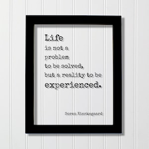 May include: A black rectangular frame containing a white print with the black typewriter-style text: Life is not a problem to be solved, but a reality to be experienced. The name Soren Kierkegaard is printed in smaller text at the bottom right.