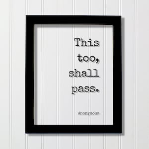 May include: A black rectangular frame containing a white print with the black typewriter-style text This too, shall pass. and the attribution Anonymous at the bottom. The design features a clean, high-contrast aesthetic with bold, legible lettering.