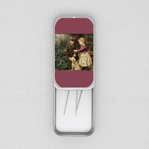 May include: A silver needle case with a hinged lid. The lid has a burgundy panel with a vintage illustration of two children and a dog near a Christmas tree. The case contains three needles.