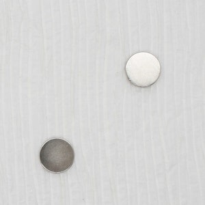 May include: Two silver round stud earrings on a white textured background.