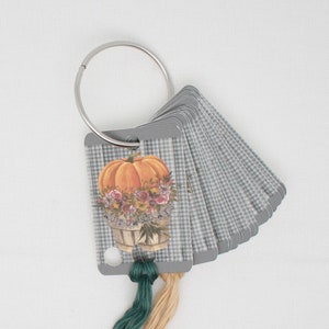 May include: A set of gray, gingham-patterned cards held together by a silver ring. The first card features a pumpkin illustration with the text "AUTUMN DAYS". Green and tan threads are attached to the bottom.
