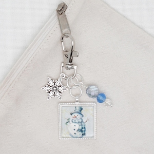 以下が含まれることがあります： 雪だるまの絵柄、雪の結晶のチャーム、青いガラスビーズが付いたシルバーのキーホルダーです。