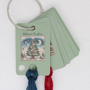 May include: A set of green cardstock tags with a silver ring, featuring a Christmas tree illustration and the text "Patchwork Christmas." The tags have blue and red embroidery floss attached. The image on the tag shows a Christmas tree, a crescent moon, and a starry sky.