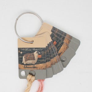 May include: A set of Halloween themed embroidery floss cards featuring a sheep wearing a pumpkin for a face. The cards are attached to a silver ring and the text "A Merry Halloween" is printed on the card.