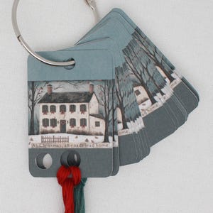 Può includere: Un set di etichette regalo a tema natalizio su un anello d'argento. Ogni etichetta presenta un dipinto ad acquerello di una casa bianca con porta e persiane rosse, alberi e la scritta "At Christmas, all roads lead home."