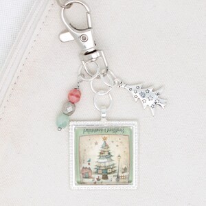 May include: A silver keyring with a Christmas-themed charm. The charm features a square image of a decorated Christmas tree, a house, and the text "Remember Christmas". Additional charms include a tree-shaped pendant and colourful beads.