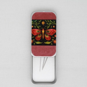 May include: A silver metal needle case with a red, black and green butterfly design on the lid. The case is open and contains three needles.