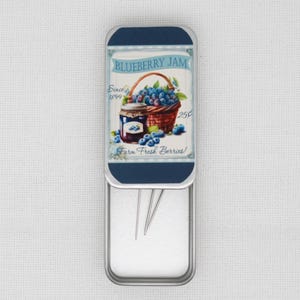 May include: A rectangular metal needle case with a hinged lid. The lid features a vintage-style illustration of blueberry jam, a basket of blueberries, and the text "Blueberry Jam" and "Farm Fresh Berries!"