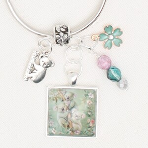 May include: Silver charm bracelet featuring koala bear and floral charms. Includes a square pendant with a koala family illustration, a koala bear charm, a flower charm, and beaded accents. A delicate piece of jewellery.