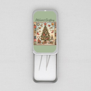 May include: An open rectangular metal tin with a light green lid. The lid displays a Christmas tree illustration with the text "Patchwork Christmas". The illustration includes a decorated tree and houses. The tin contains sewing needles.