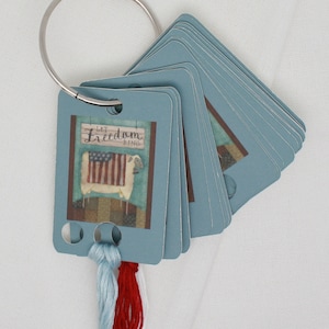 May include: A blue card holder with a patriotic sheep design and the text "Let Freedom Ring". The card holder has three holes for holding floss or thread.