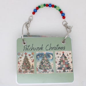 以下が含まれることがあります： 「Patchwork Christmas」の文字と3つのクリスマスツリーのイラストが描かれた、緑色の正方形のメモ帳。 赤、青、緑のビーズが付いたビーズのハンドルが付いています。 金属製のリングでまとめられています。