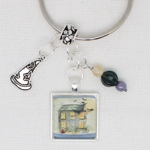 May include: A silver charm bracelet featuring a witch's hat charm, a square pendant with a spooky house illustration, and decorative beads. Ideal for Halloween, this bracelet adds a touch of festive flair to any outfit.