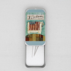 May include: A rectangular metal needle case with a patriotic design. The lid features a sheep with an American flag design and the words "Let Freedom Ring." The case is open, revealing several needles.