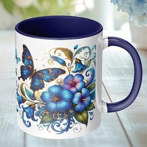 May include: A white ceramic mug with a blue interior and a colorful floral design featuring blue butterflies and flowers. The mug has a blue handle.
