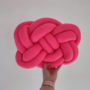 Könnte beinhalten: Ein knallpinkes, geknüpftes Kissen mit einem einzigartigen gewebten Design. Das Kissen ist weich und flauschig und perfekt, um jedem Raum einen Farbtupfer zu verleihen.