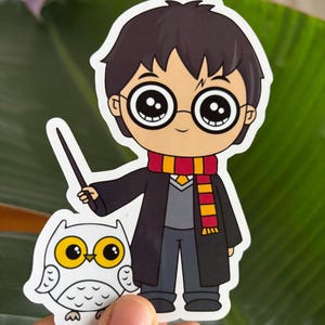 May include: A cartoon illustration of Harry Potter, a young wizard with black hair and glasses, wearing a black robe with a red and yellow scarf. He is holding a wand in his right hand and standing next to a white owl with yellow eyes.