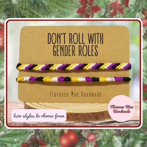 May include: Two handmade woven bracelets featuring a non-binary pride color pattern of yellow, white, purple, and black stripes. The bracelets are displayed on a tan card with the text DON'T ROLL WITH GENDER ROLES and Florence Mae Handmade.