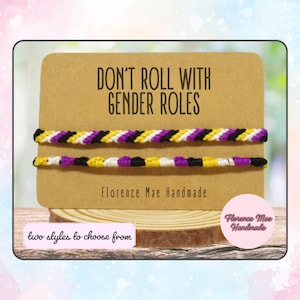 May include: Two friendship bracelets with a yellow, black, white, and purple color scheme. The bracelets are displayed on a brown card with the text "Don't Roll With Gender Roles" and "Florence Mae Handmade".