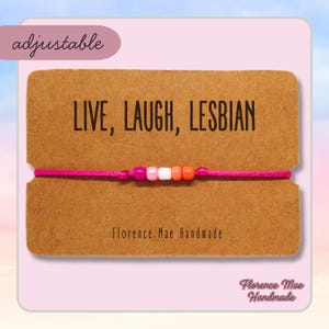 May include: A pink and orange beaded bracelet with the text "LIVE, LAUGH, LESBIAN" on a brown card. The card also says "Florence Mae Handmade".