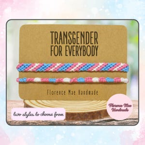 May include: Two handmade friendship bracelets in the colors of the transgender flag, blue, pink, and white. The bracelets are displayed on a brown card with the text "TRANSGENDER FOR EVERYBODY" and "Florence Mae Handmade".