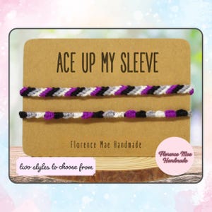 May include: Two friendship bracelets with the text "ACE UP MY SLEEVE" and "Florence Mae Handmade" on a brown card. The bracelets are black, white, gray, and purple.